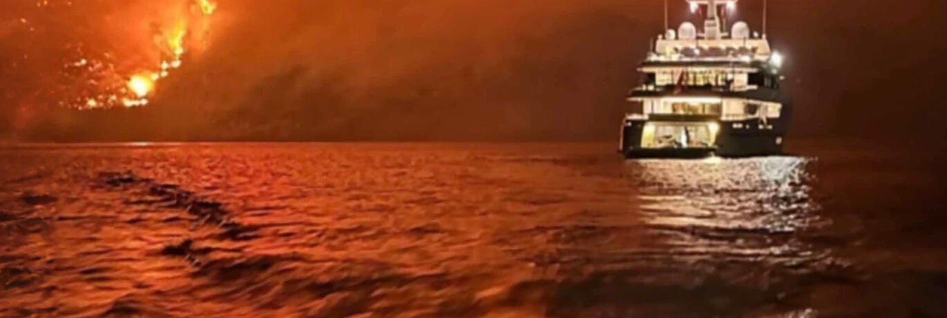 Superyacht against backdrop of fire
